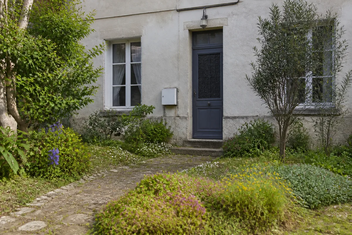Massif de plantes basses et arbustes latéraux devant une façade de maison, avec porte et fenêtres dégagées
